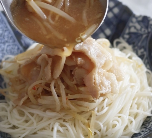 器に盛り付けられたそうめんの上に、レンジで加熱した豚バラ肉ともやしの具材と味噌だれが、おたまを使ってたっぷりと掛けられている様子。豚バラもやしの味噌だれそうめんの盛り付け。