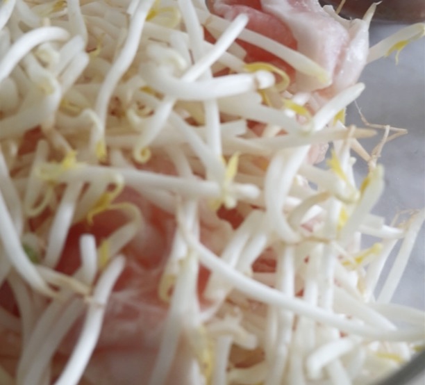 耐熱ボウルの中に、食べやすい大きさにカットされた豚バラ薄切り肉と新鮮なもやしが交互に重ねて入れられている様子。レンジで簡単！豚バラもやしの味噌だれそうめんの具材準備。