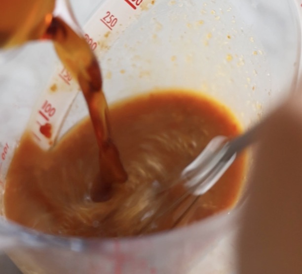 計量カップの中で、味噌、豆板醤、にんにく、めんつゆが泡立て器でよく混ぜ合わされている様子。豚バラもやしの味噌だれそうめんの美味しいタレが完成していく工程。