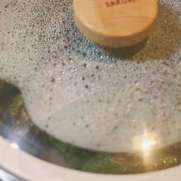フライパンに蓋をして、ピーマンを蒸し焼きにしている様子。蓋の内側は蒸気で曇っている。