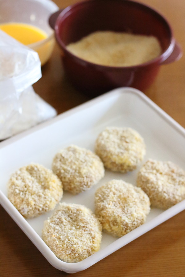 バットに並べられた衣をつけたカレーコロッケと、奥に溶き卵とパン粉