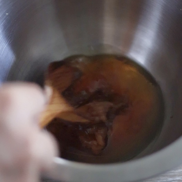 ボウルの中でめんつゆとごま油、水、ほぐした梅干しを木製スプーンで混ぜ合わせている様子。梅和えの味のベース作り
