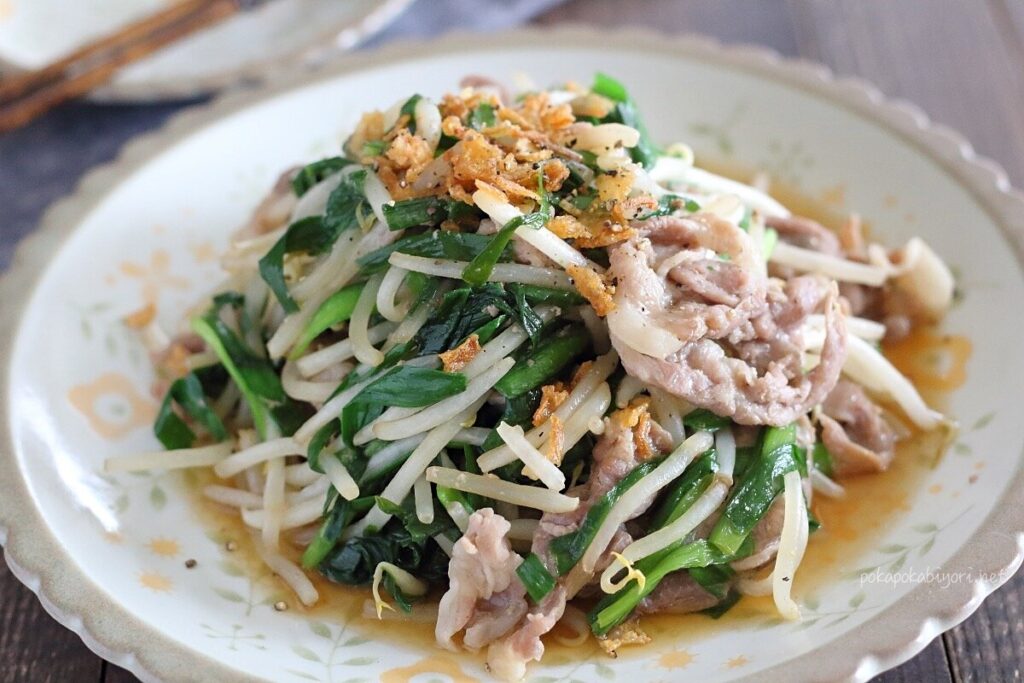 豚肉とニラともやしを電子レンジで調理した、食欲をそそるニラもやし炒めの完成品。フライドオニオンと粗挽き胡椒が添えられ、白い皿に盛り付けられている