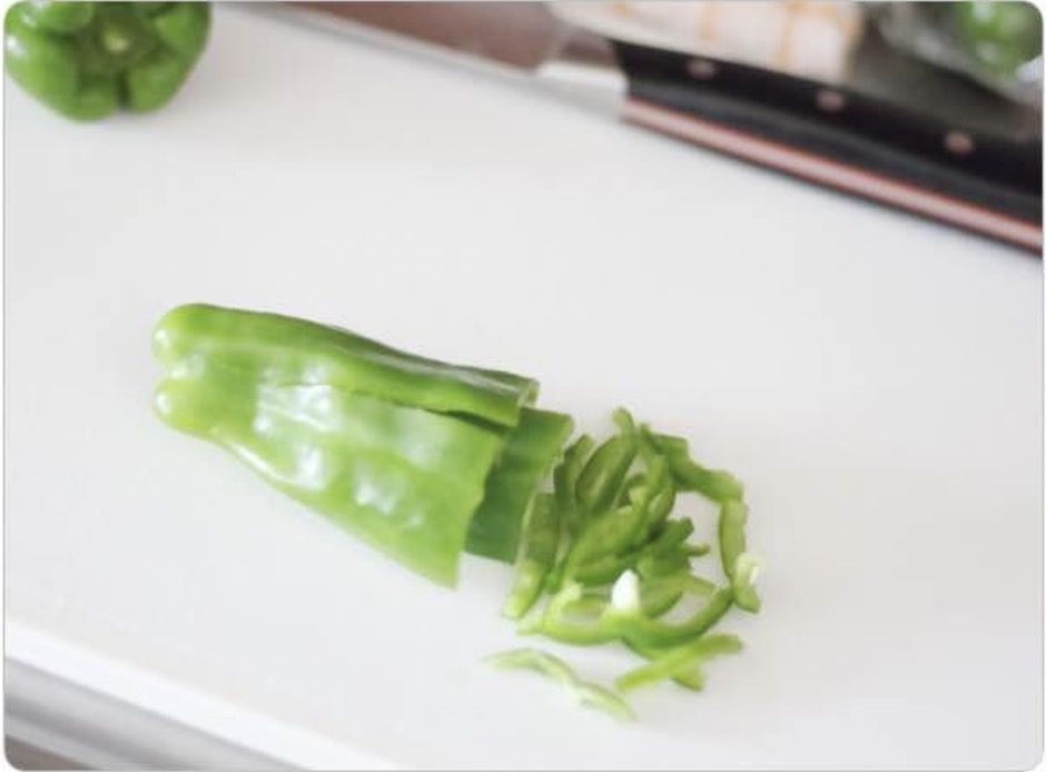 白いまな板の上で細切りにされた緑のピーマンと、カット前のピーマン。マヨネーズカレーチャーハンの具材準備。