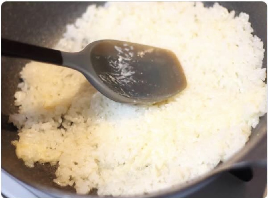 黒いフライパンの中で、ヘラを使って炒められている白いご飯と溶けたマヨネーズ。ご飯をほぐしながらマヨネーズと混ぜ合わせる工程