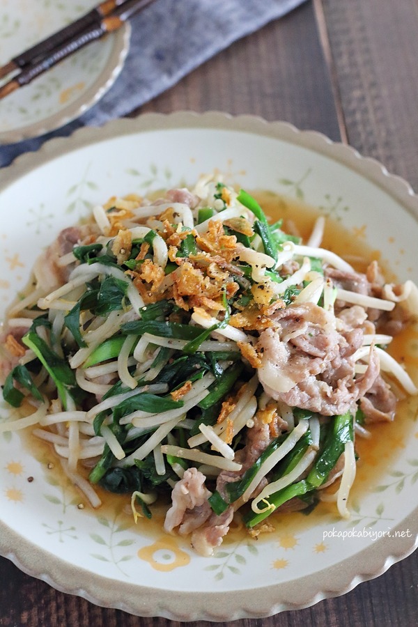 豚肉とニラともやしを電子レンジで調理した、食欲をそそるニラもやし炒めの完成品。フライドオニオンと粗挽き胡椒が添えられ、白い皿に盛り付けられている。