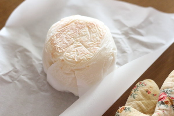 片面が焼き上がった米粉パンをクッキングシートごと鍋から取り出し、裏返してもう片面を焼く準備をしている様子。