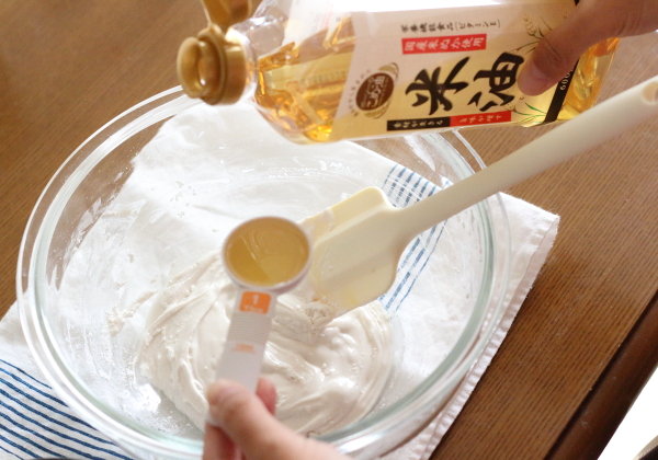米粉パンの生地に米油大さじ1を加えて混ぜる様子。ふわふわ食感を作るための油分。奥には米油のボトルとSTAUBの小鍋