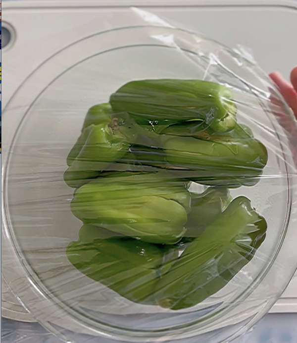 緑のピーマンがラップをかけられた透明なボウルに入っている様子