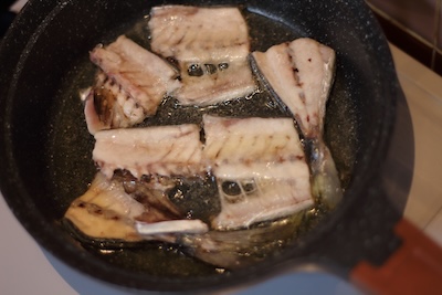 フライパンの中でアジの中骨が加熱され、表面に少し焼き色がつき始めている状態。