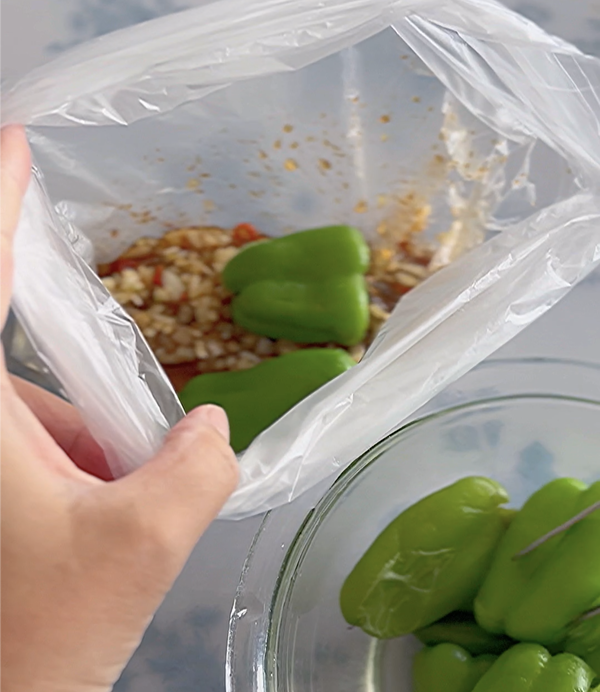 ポリ袋に加熱したピーマン、みじん切りの玉ねぎ、調味料が入っており、手で袋の上部を持っている様子