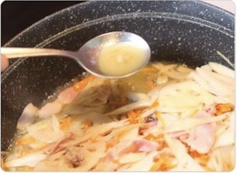 フライパンで炒めている白いきんぴらの具材に、スプーンで白ワインビネガーを加えて酸味を飛ばしている様子