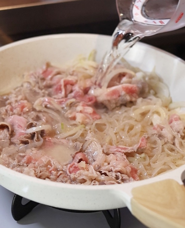 炒めた牛丼の具材に、計量カップから水を注ぎ入れている調理工程