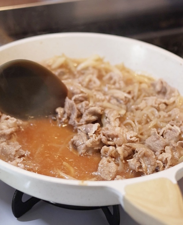牛丼の具材をフライパンで炒め煮にし、スプーンで混ぜている様子