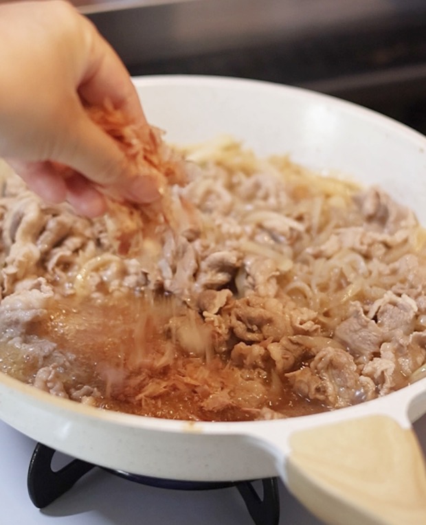 仕上げに、煮えている牛丼の具の上から手でかつお節を振りかけているところ