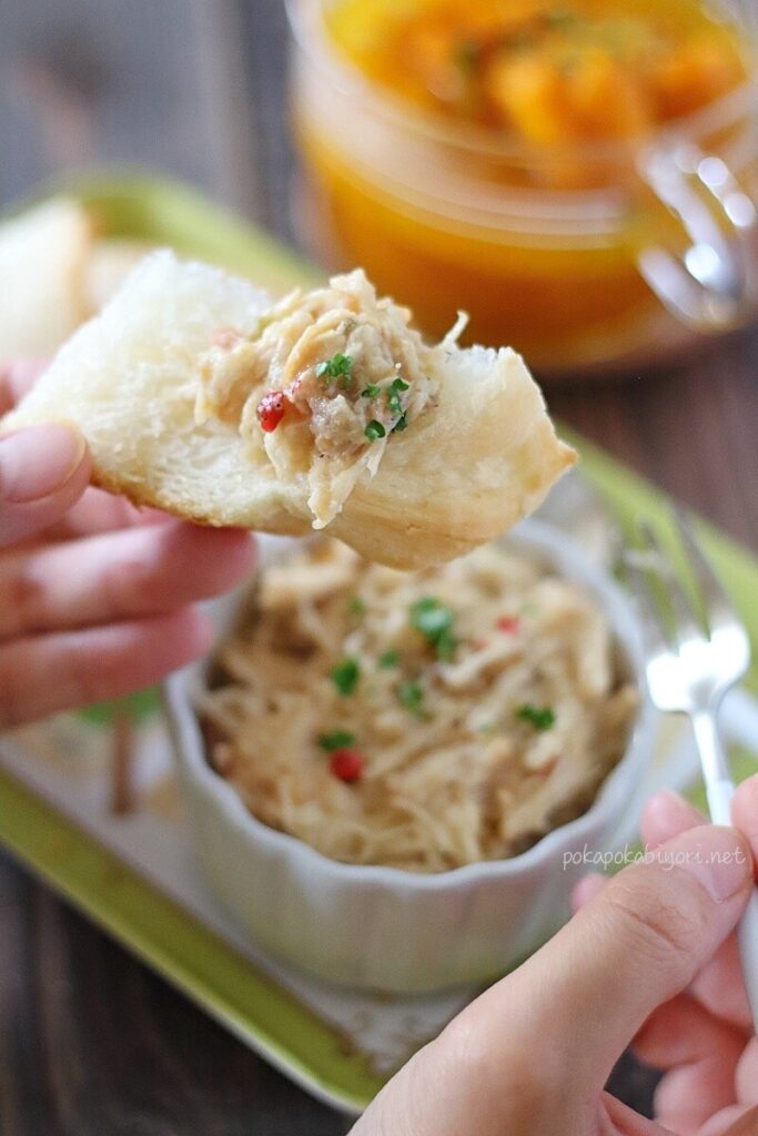 トーストしたバゲットに、完成した里芋と鶏むね肉のリエット風ディップを乗せ、フォークで食べようとしている手元の写真。ワインのおつまみやパンのお供に。