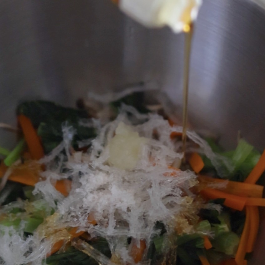 加熱した小松菜とにんじんが入ったボウルに、糸寒天と調味料を加えて味付けしているところ