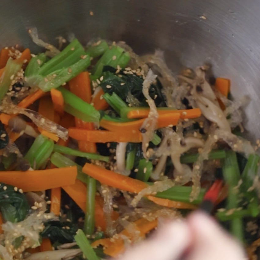 小松菜とにんじんのナムルの材料をボウルの中で箸を使って全体をよく混ぜ合わせている様子
