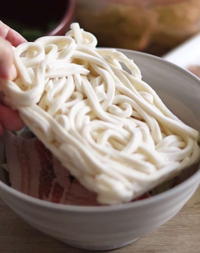 レンジで簡単な豚バラ旨塩うどん。豚肉と野菜の上に冷凍うどんをそのまま乗せて加熱準備をする場面