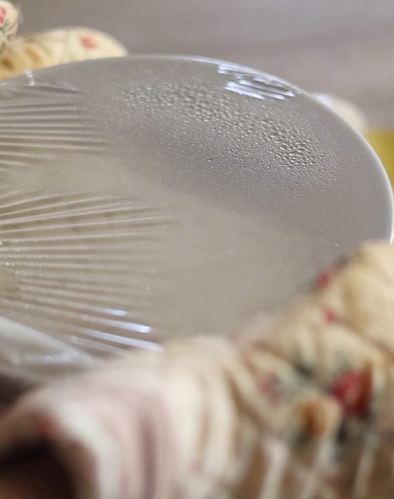 加熱調理後の豚バラ旨塩うどん。湯気で曇ったラップがかかった熱々のうどん鉢を、鍋つかみを使ってレンジから取り出す工程