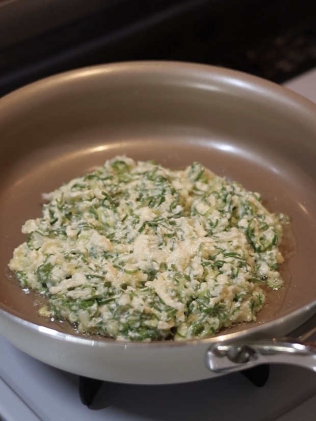フライパンに油をひき、ねぎがたっぷり入った豆腐お好み焼きの生地を円形に広げて焼いているところ。