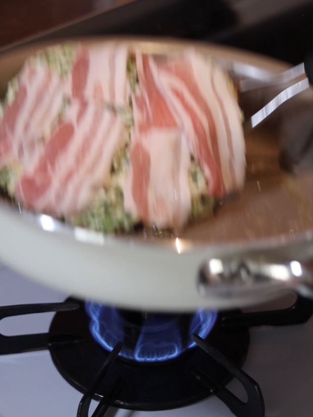 片面を焼いたお好み焼きの生地の上に、豚バラ薄切り肉をきれいに広げてのせている調理シーン。
