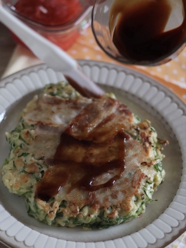 皿に盛り付けられた焼き立ての豆腐お好み焼きに、刷毛でお好み焼きソースを塗って仕上げている完成間近の写真。