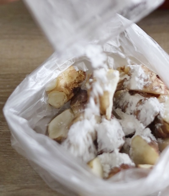 ポリ袋に入れたカット済みの菊芋に、片栗粉とオリーブオイルを加えて袋を振り、全体になじませている工程