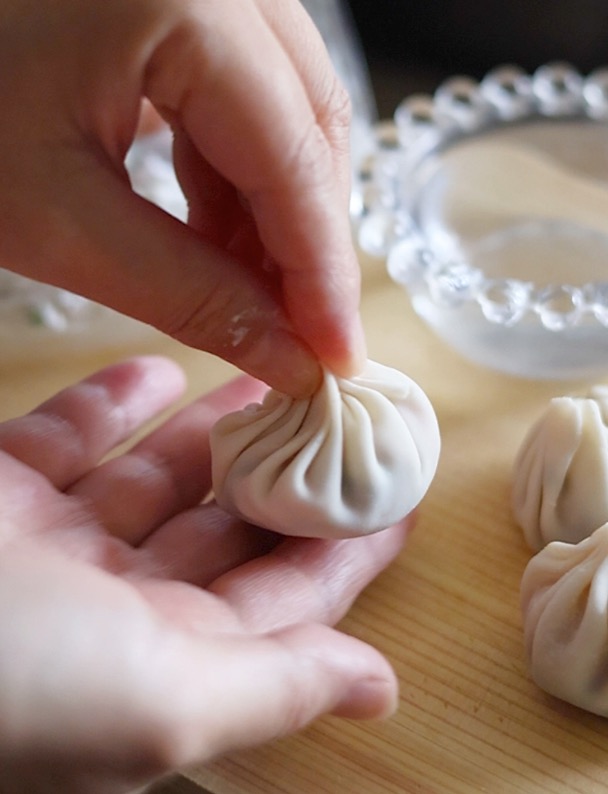 大判餃子の皮の縁に水をつけ、ヒダを寄せながら包みこみ、上部の口をしっかりと閉じる。