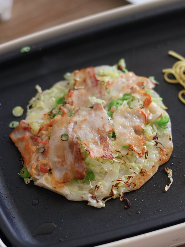 ホットプレートで焼いた広島焼きの豚肉に焼き色がついたらひっくり返します。