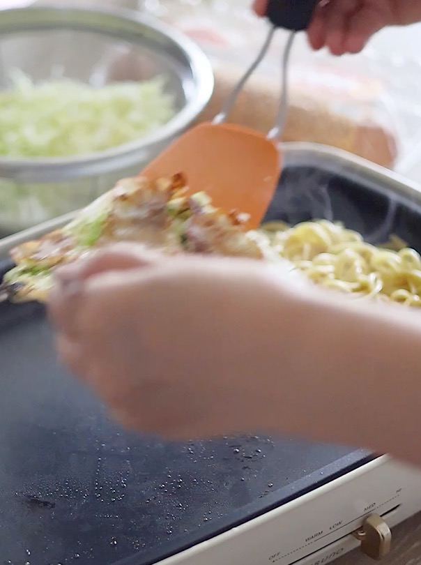 麺の上に具材をのせ、さらにその横で焼いた目玉焼きの上に全体をスライドさせて合体させます。