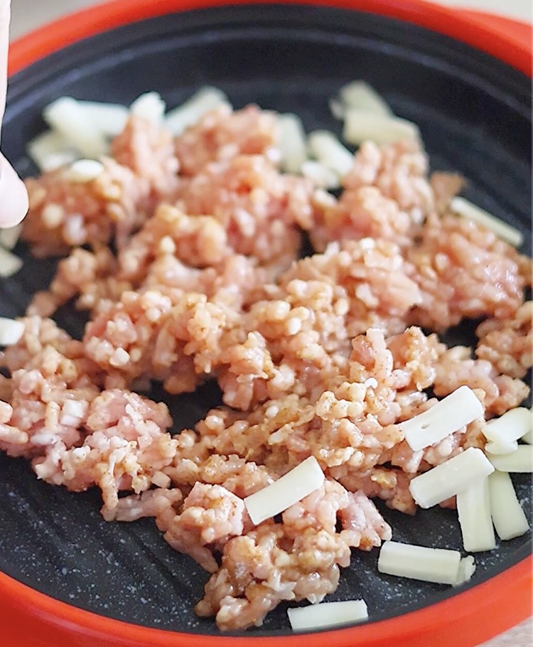 電子レンジ用焼き物調理器の中心に、調味料を混ぜた豚ひき肉を平らに広げるようにして置きます。その周囲を囲むようにピザ用チーズを散らします。